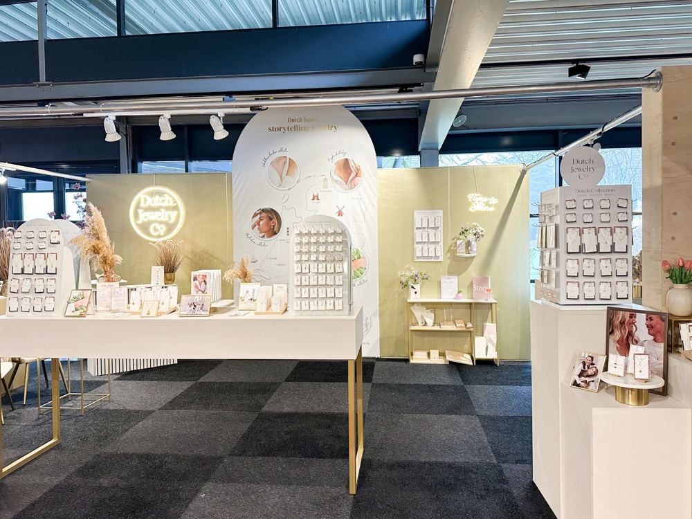 Opgebouwde beursstand van Dutch Jewelry Company met neonlogo, displays en droogbloemen