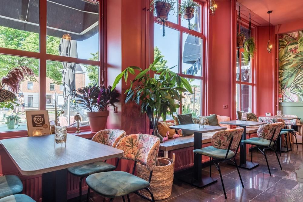 Interieur van Royaal Belegd in Sneek met roze wanden, planten en bloemenstoelen